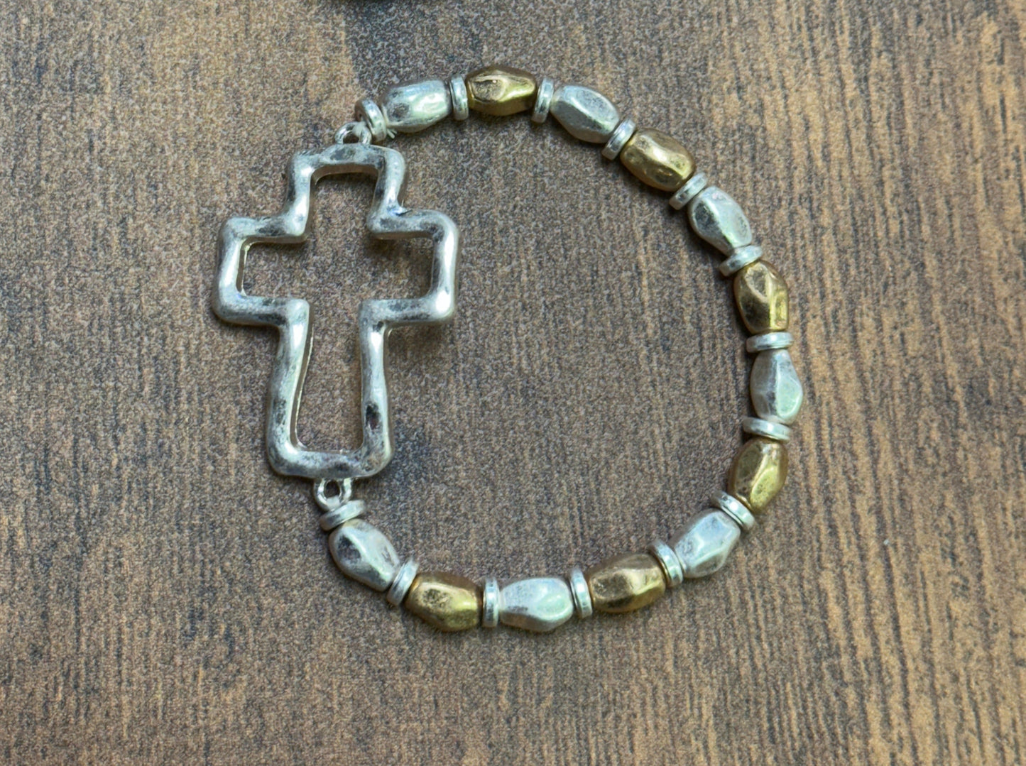 silver and gold beaded bracelet with cross designs on a wooden surface