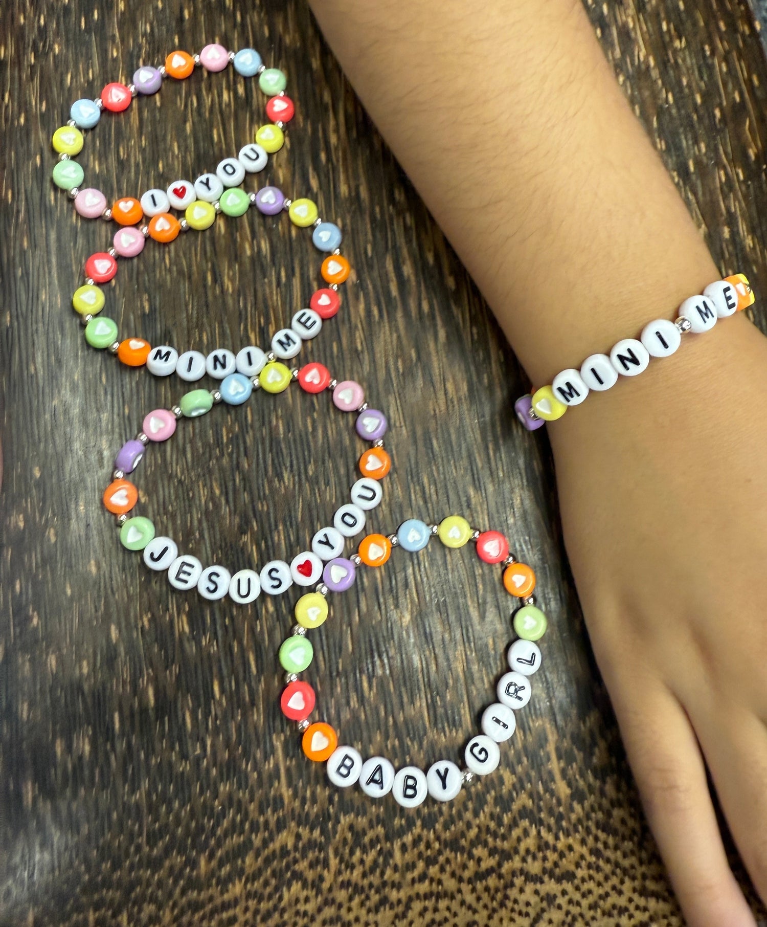 Colorful children's beaded bracelets on a wooden surface with a hand wearing one of the bracelets.