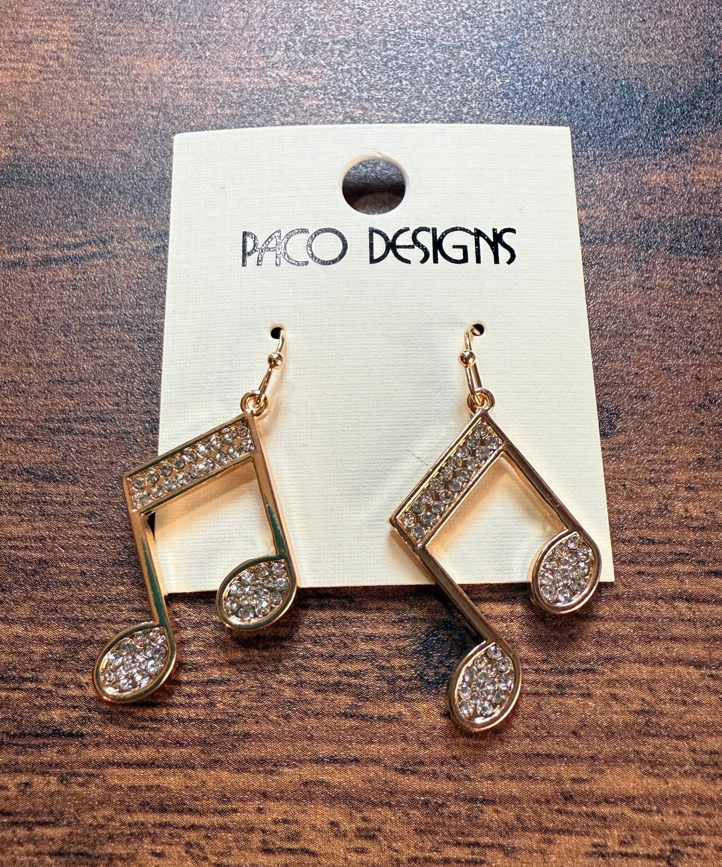 Gold music note earrings with rhinestones on a Paco Designs card against a wooden background