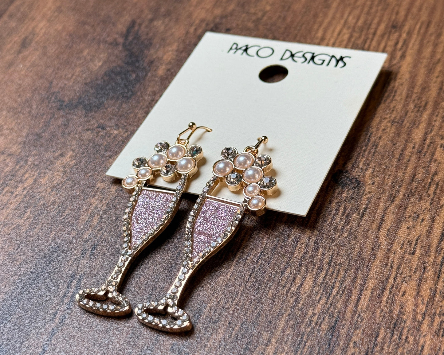 Earrings on a display card with 'Paco' branding on a wooden surface