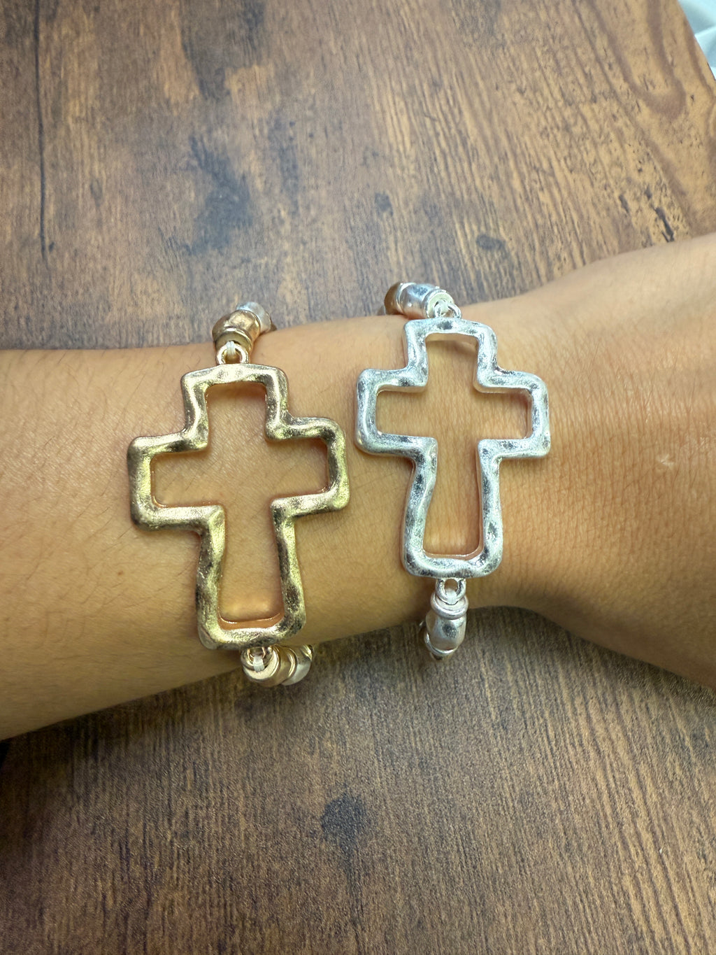 gold and silver Bracelet with cross design on a wrist against a wooden background