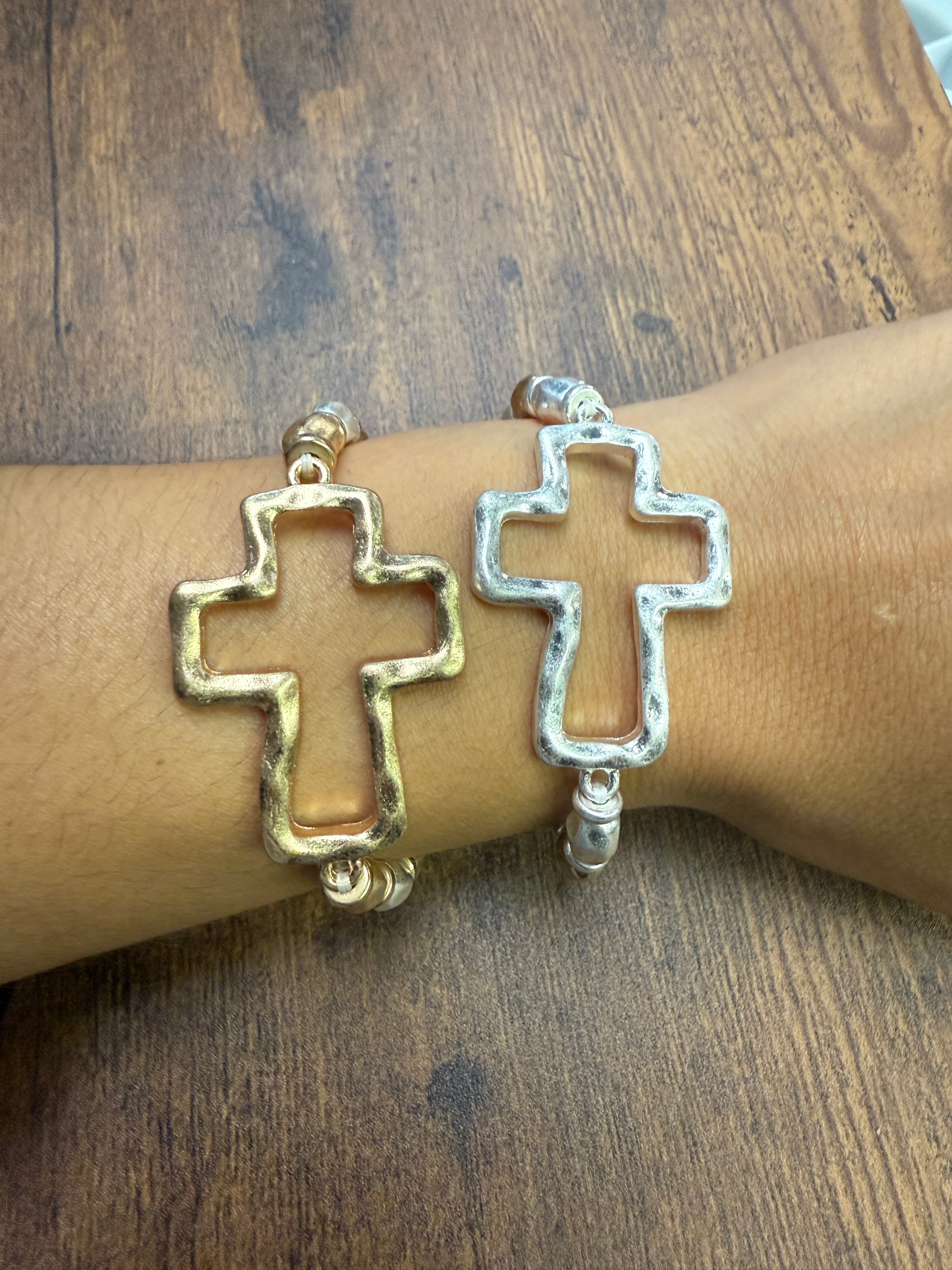 gold and silver Bracelet with cross design on a wrist against a wooden background