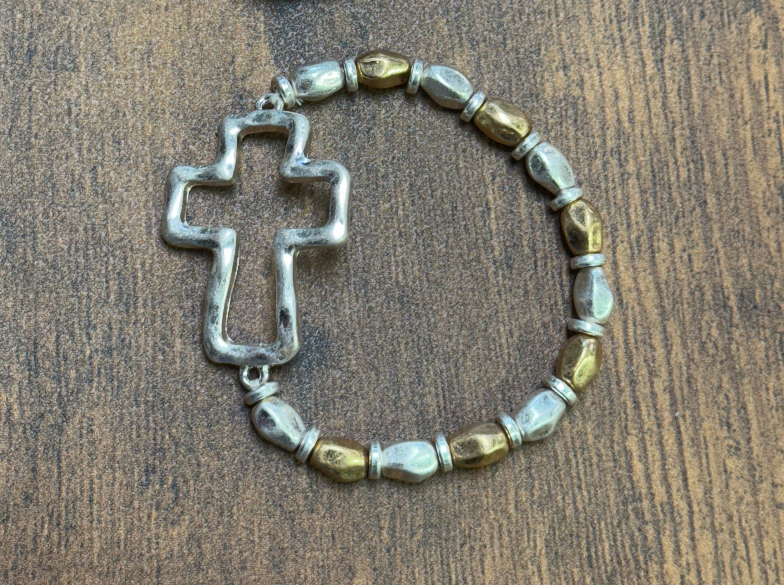silver and gold beaded bracelet with cross designs on a wooden surface