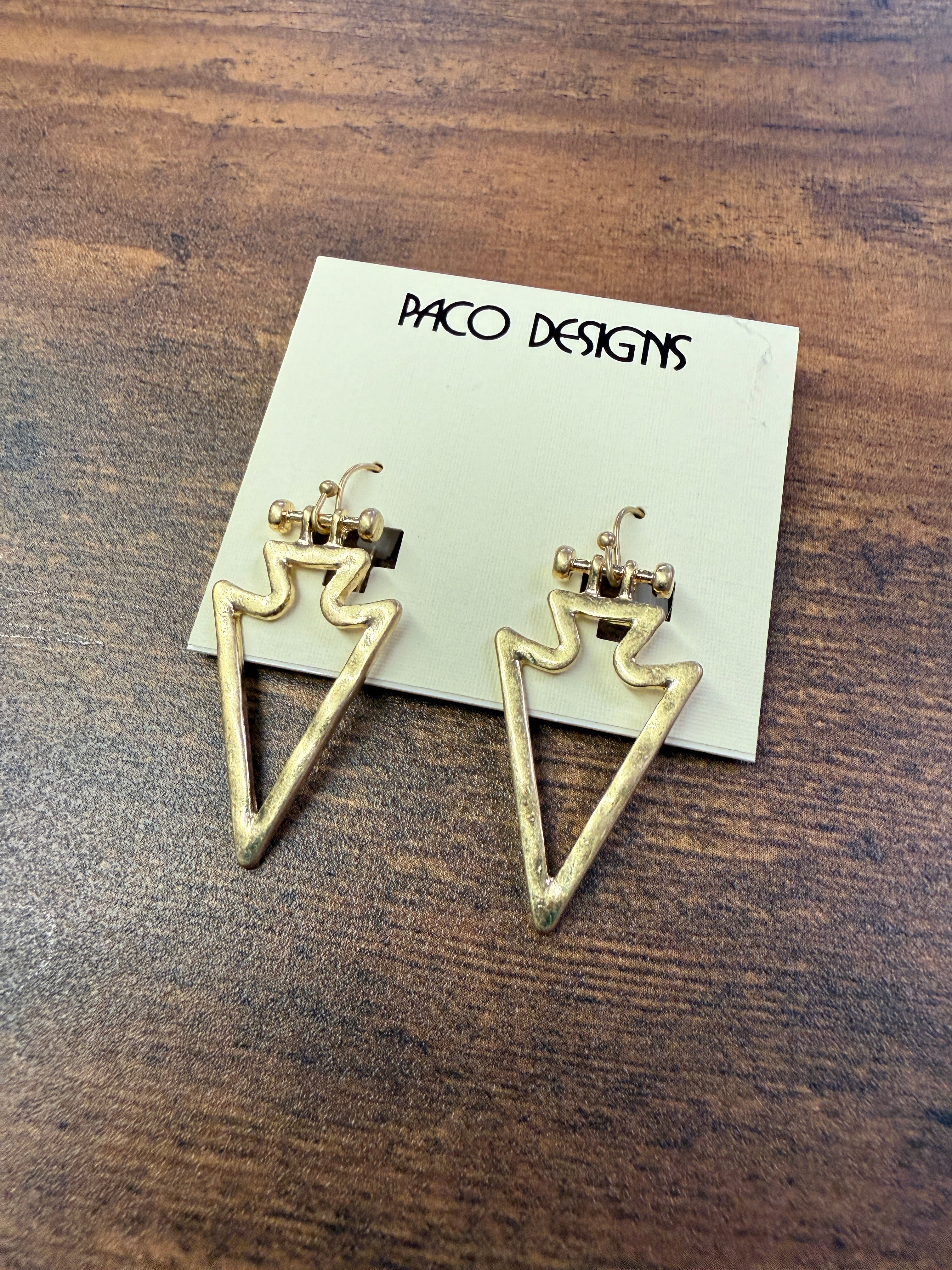 Gold triangle-shaped earrings on a wooden surface with 'Paco Designs' card.