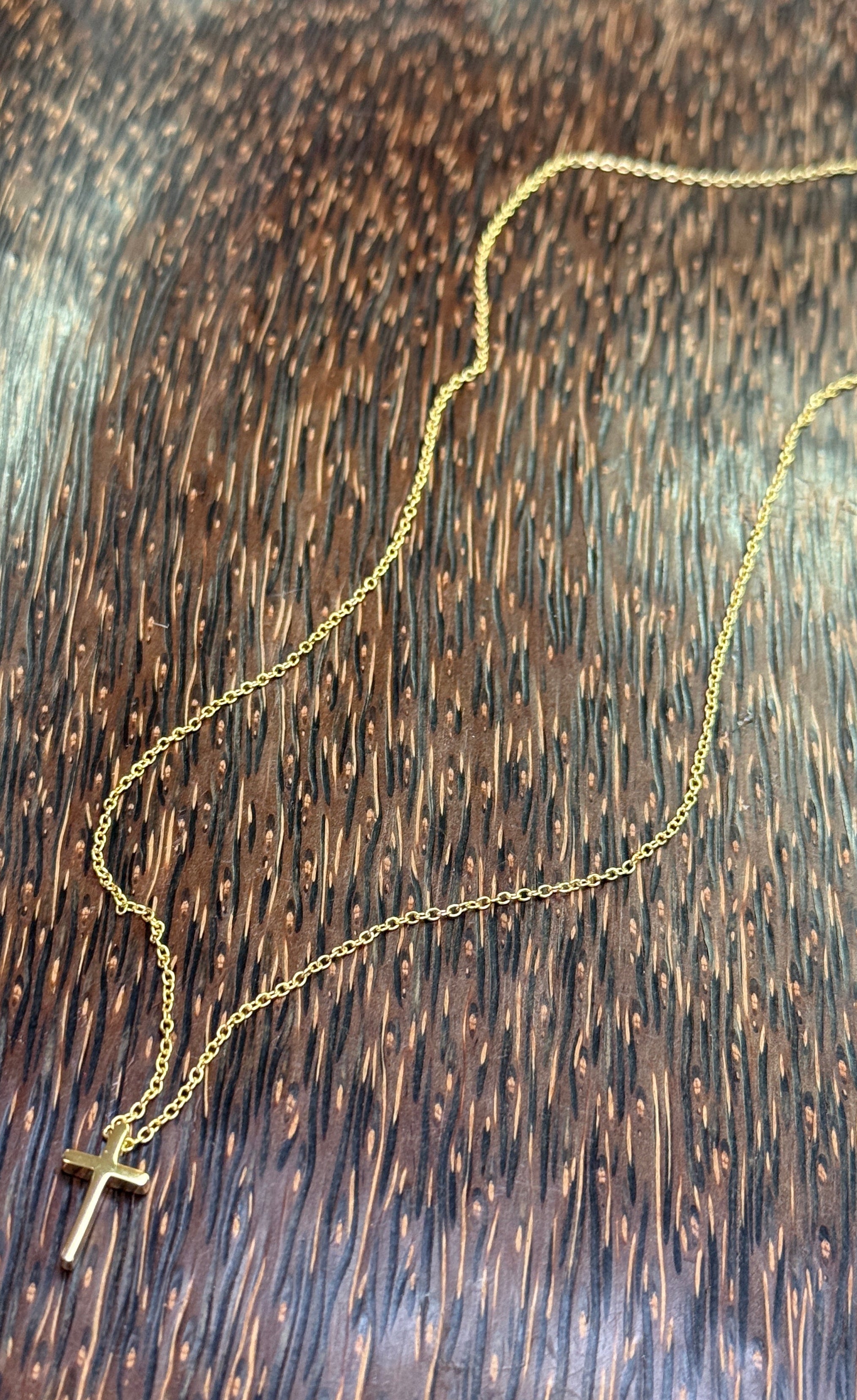 Gold necklace with a cross pendant on a wooden surface