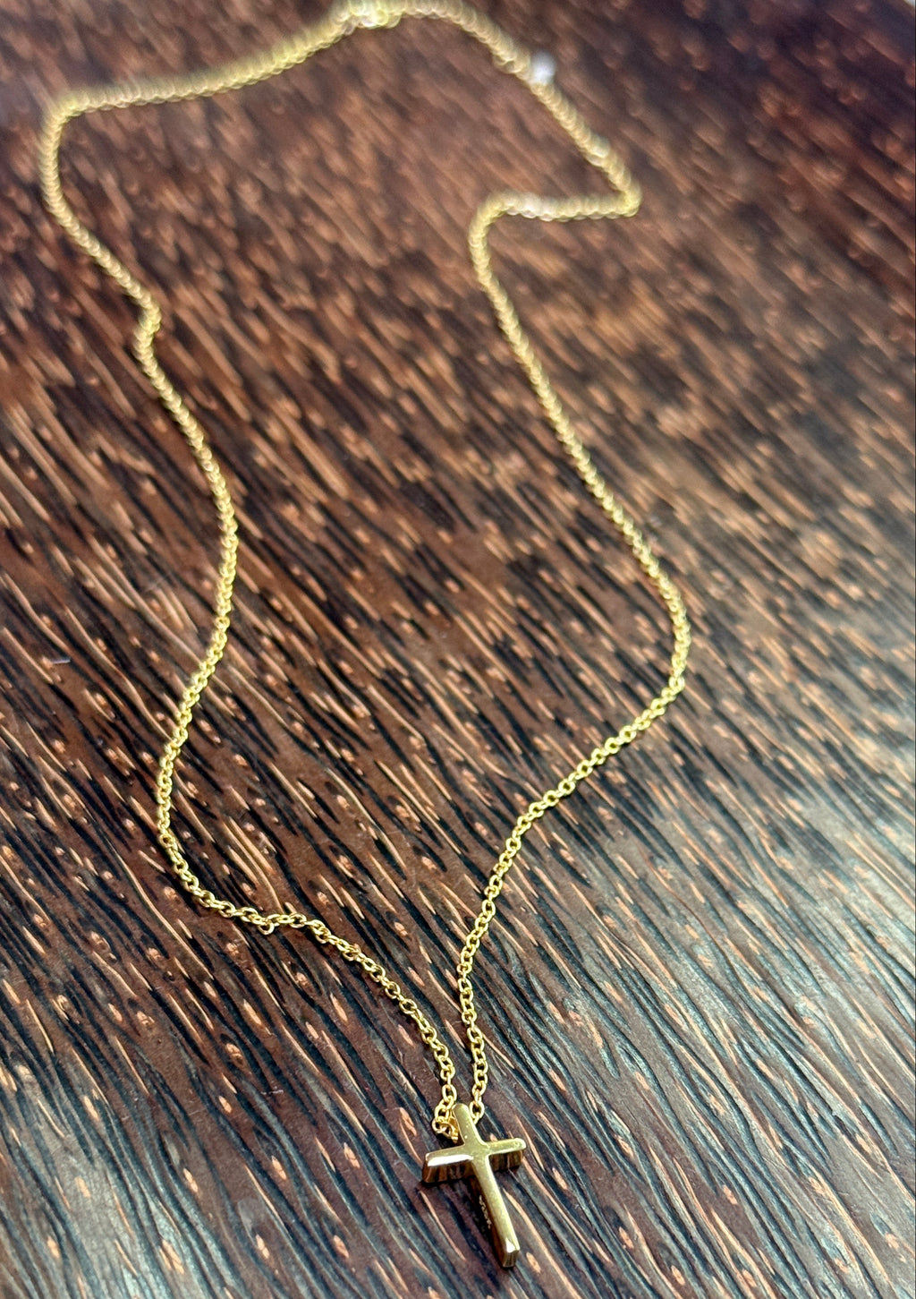 Gold necklace with a cross pendant on a wooden surface