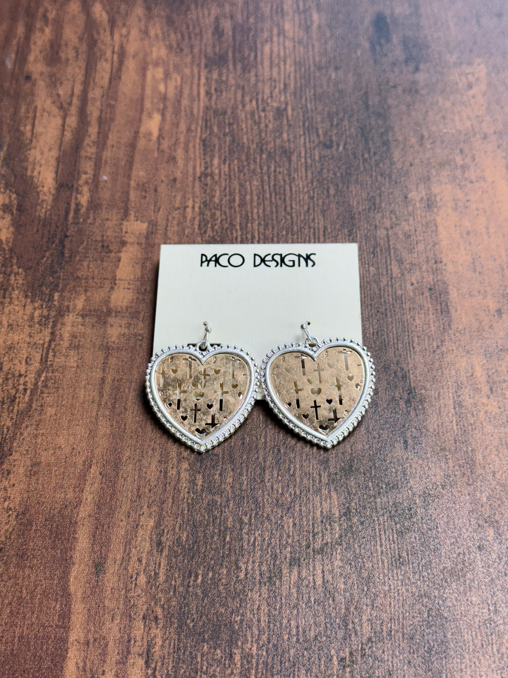 Heart-shaped earrings on a wooden surface with a card labeled 'Paco Designs'.