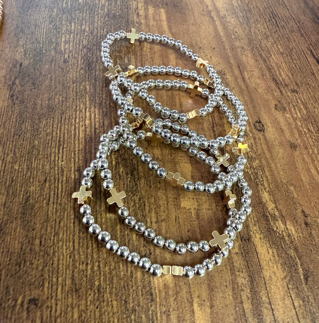 Silver beaded bracelets with gold crosses on a wooden surface