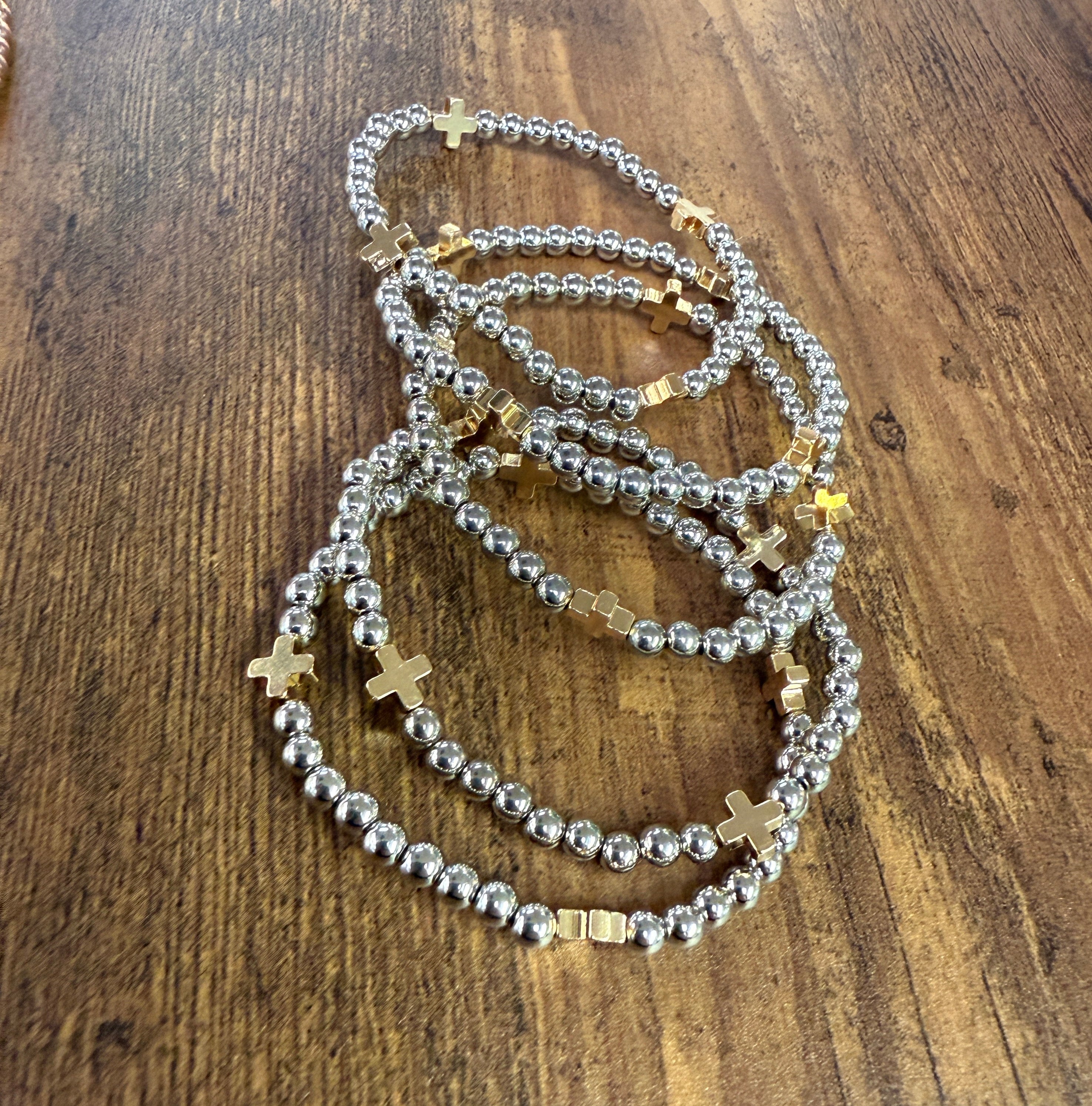 Silver beaded bracelets with gold crosses on a wooden surface
