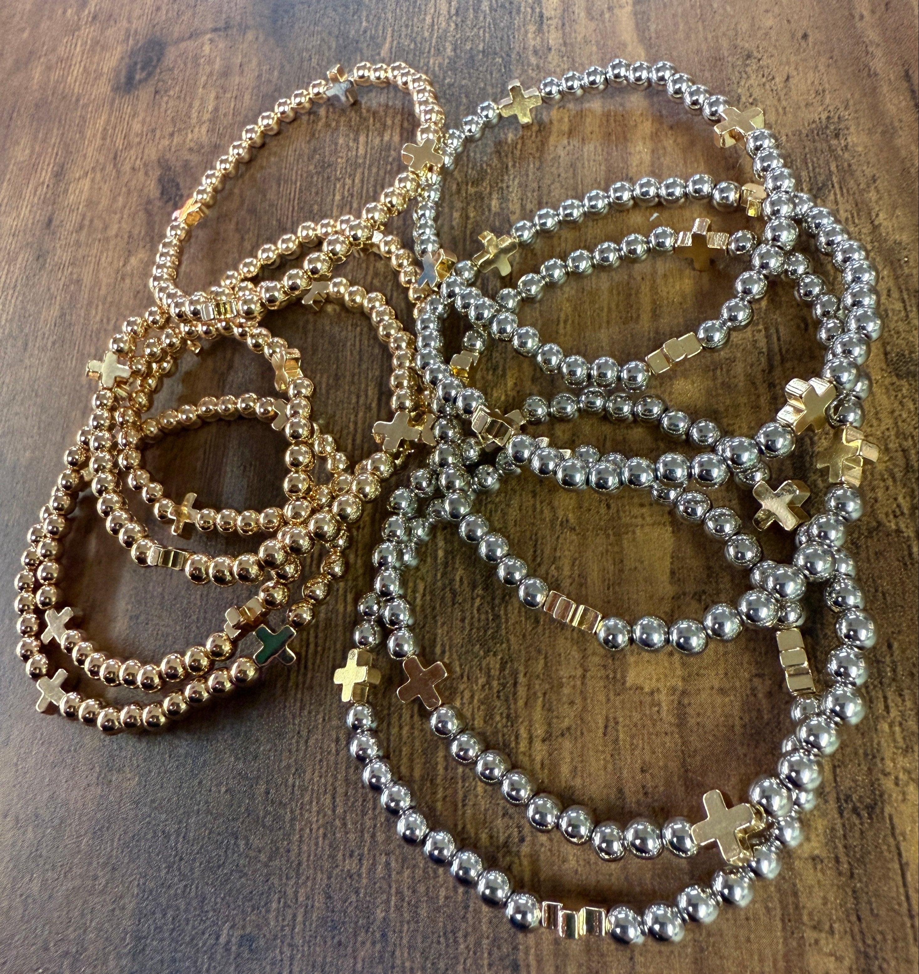 Silver and gold beaded bracelets with a gold cross accent on each bracelet on a wooden surface