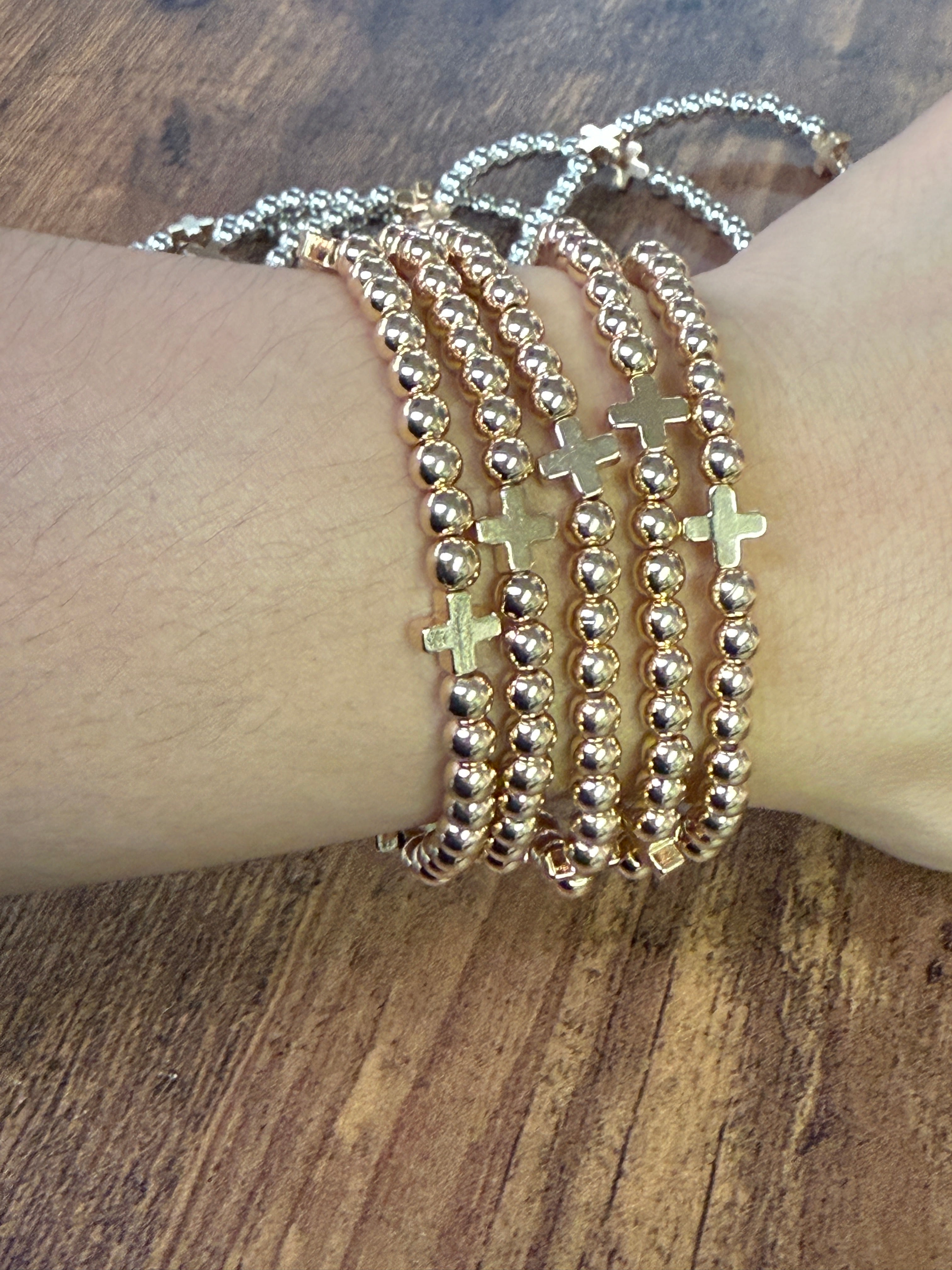 Multiple bracelets with beads and crosses on a wrist against a wooden background