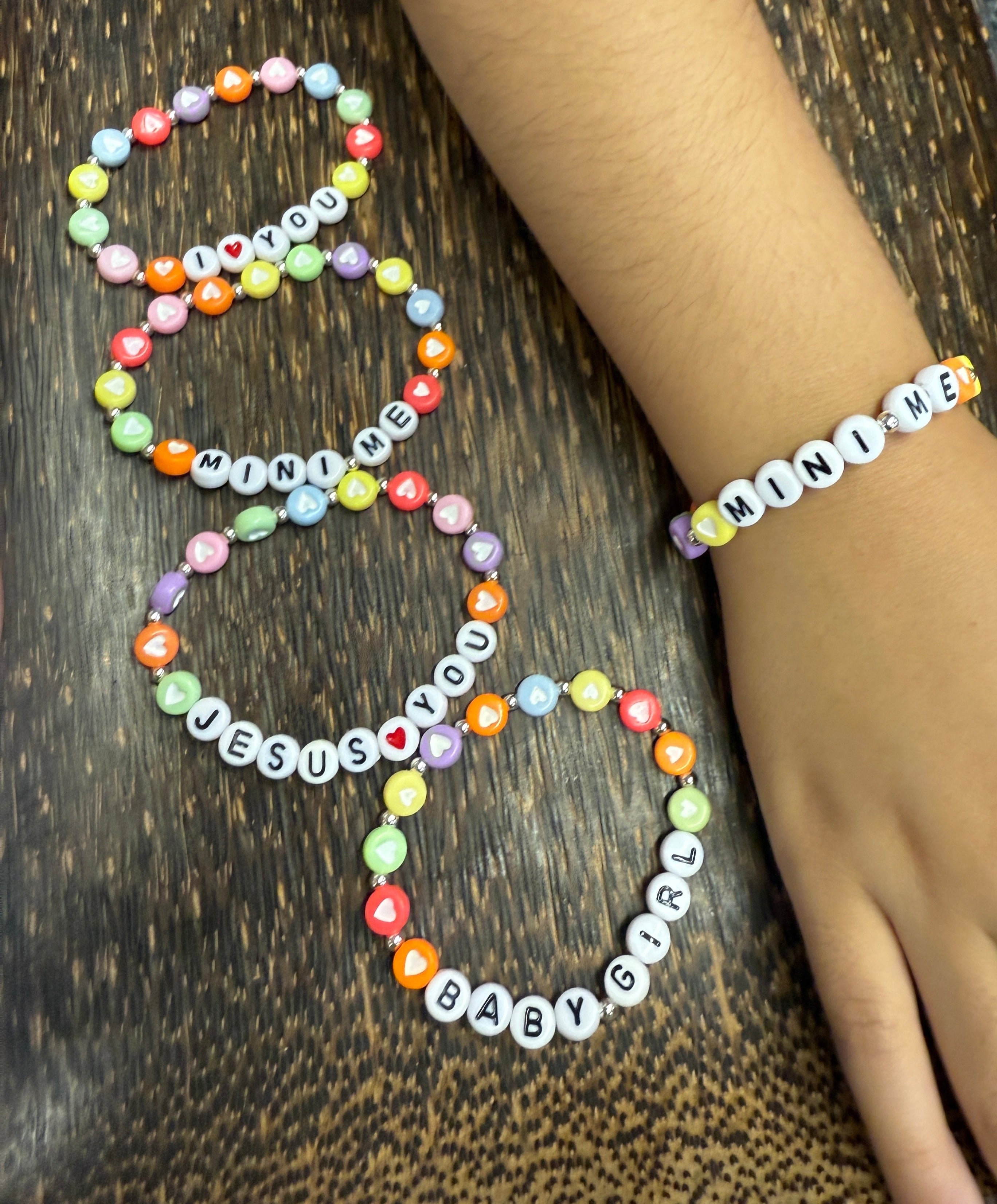 Colorful children's beaded bracelets on a wooden surface with a hand wearing one of the bracelets.