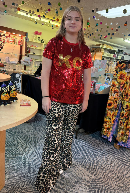 Person wearing a red sequin top size small and leopard print pants size small standing in a store with colorful fabric displays.