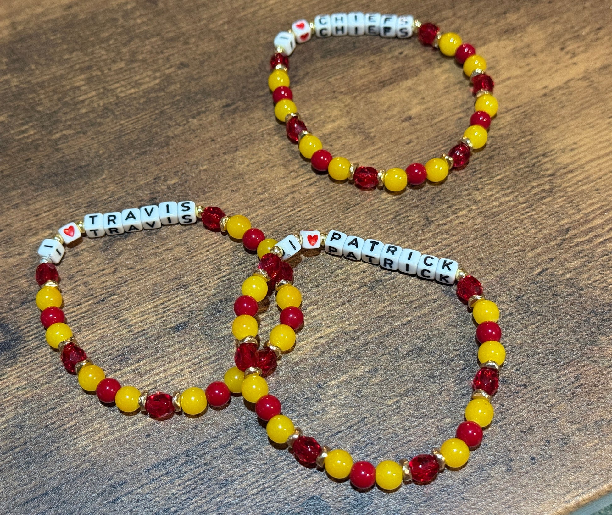 Two beaded bracelets with name charms on a wooden surface