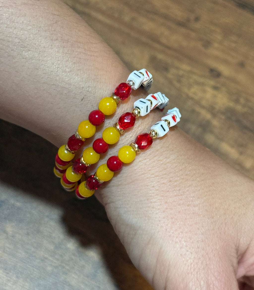 Hand wearing three beaded bracelets with red, yellow, and white beads on a wooden surface.