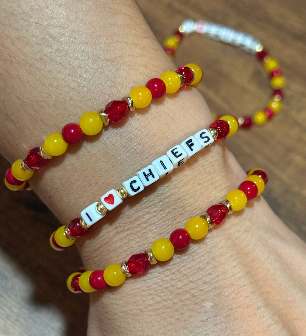 Bracelets with red and yellow beads and a 'Chiefs' tag on a wrist against a wooden background