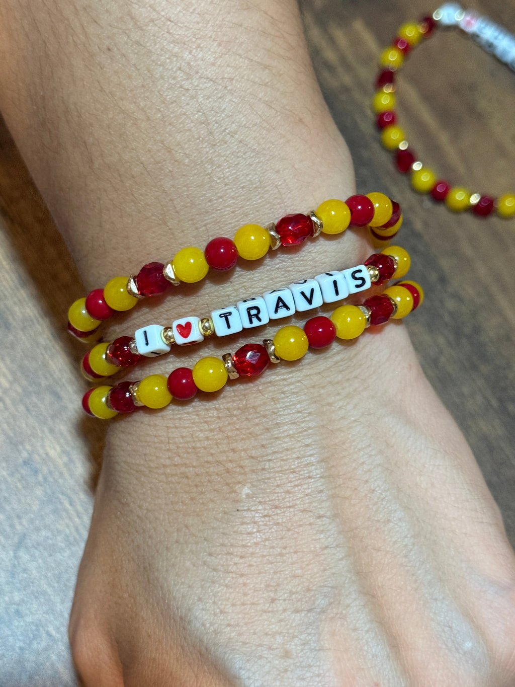 Bracelets with red, yellow, and white beads on a wrist against a wooden background