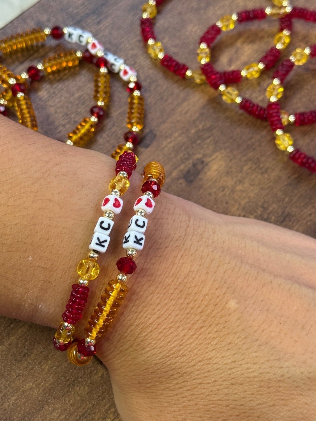 Beaded bracelet with letter beads on a wrist, with more beaded bracelets in the background.