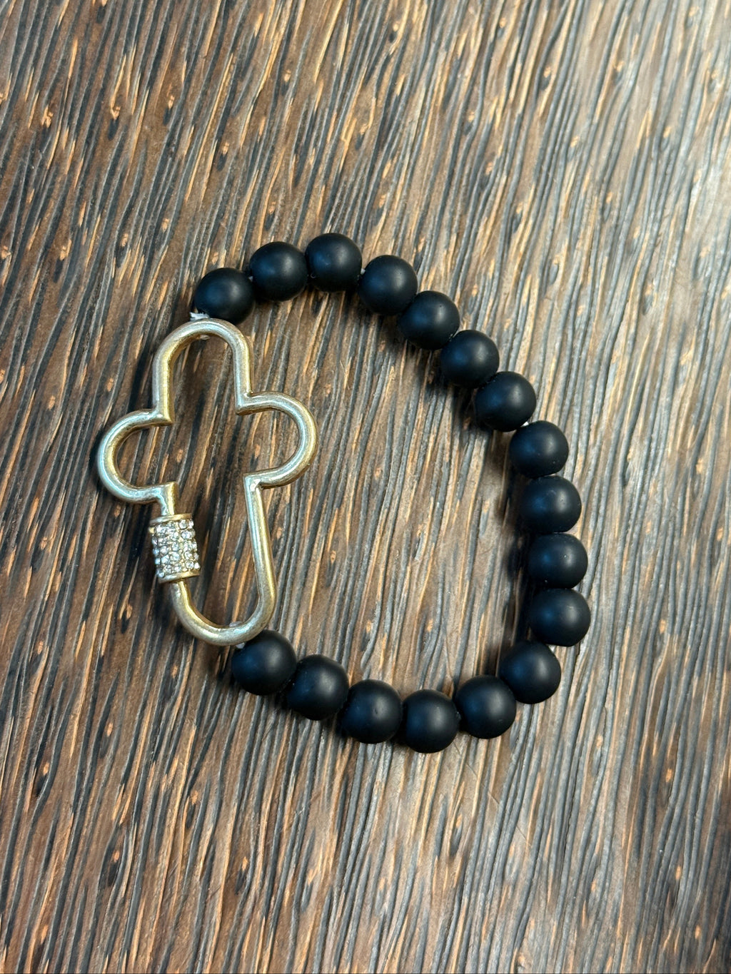 Black beaded bracelet with a metal cross pendant on a wooden surface