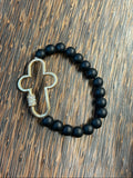 Black beaded bracelet with a metal cross pendant on a wooden surface