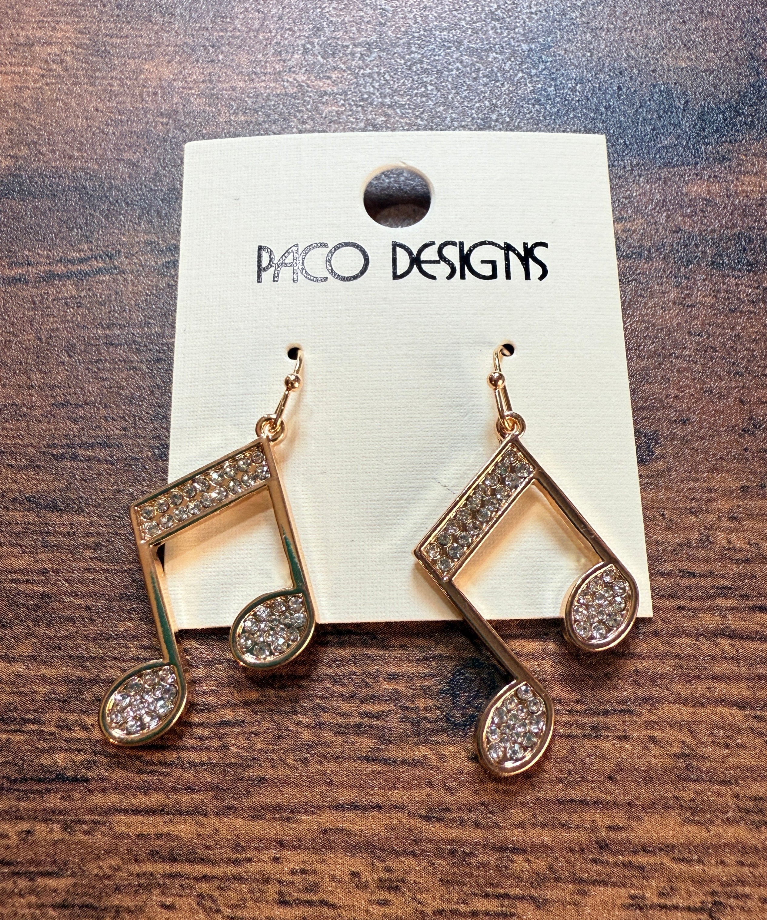 Gold music note earrings with  rhinestones on a Paco Designs card against a wooden background