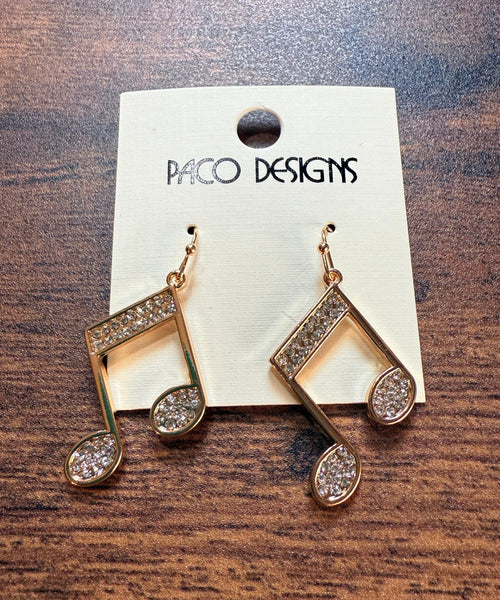 Gold music note earrings with  rhinestones on a Paco Designs card against a wooden background