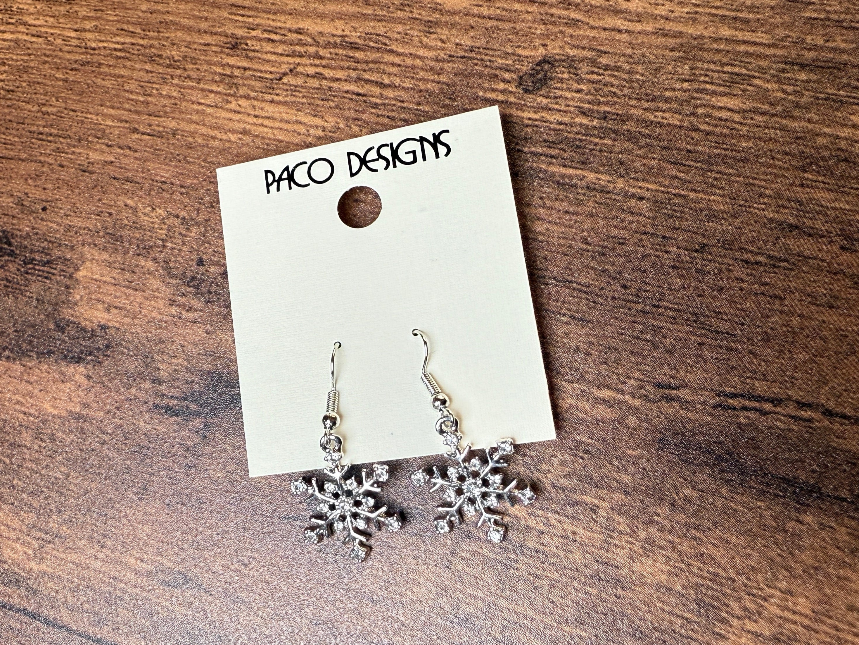 Snowflake earrings on a Paco Designs card on a wooden surface
