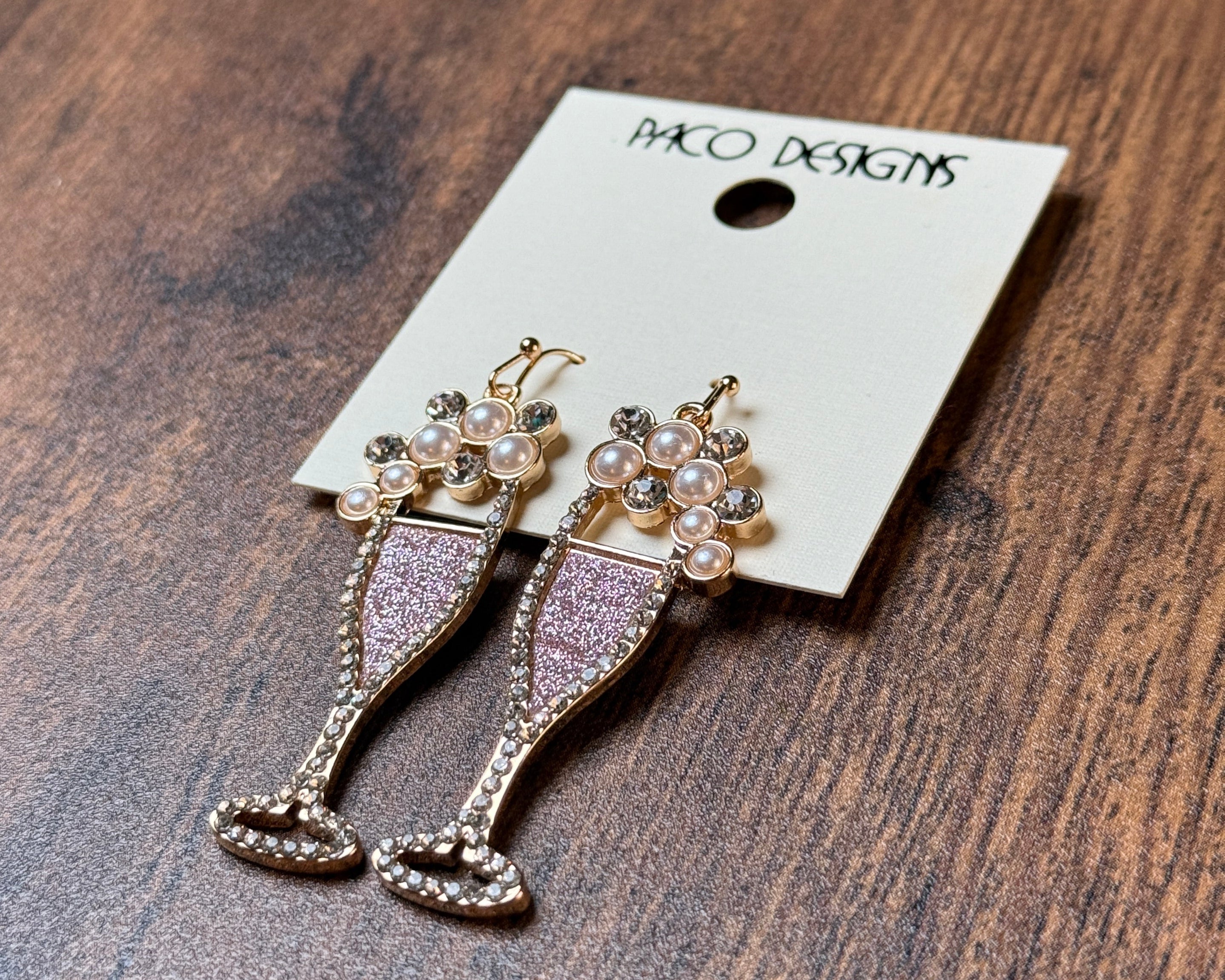 Earrings on a display card with 'Paco' branding on a wooden surface