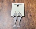Silver earrings with a decorative design on a branded card, placed on a wooden surface.