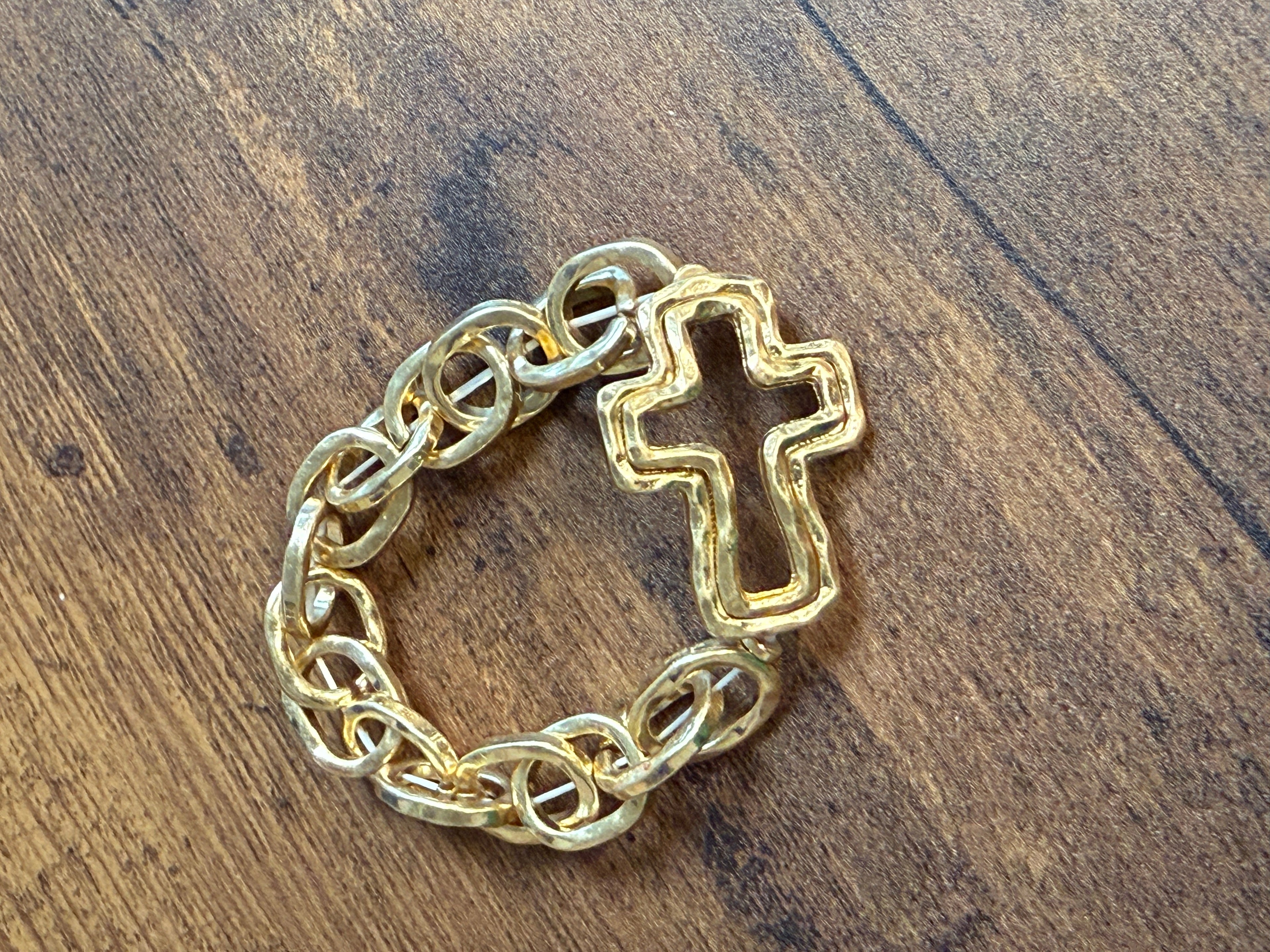 Gold chain bracelet with a cross charm on a wooden surface