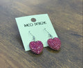 Heart-shaped earrings on a Poco Designs card against a wooden surface