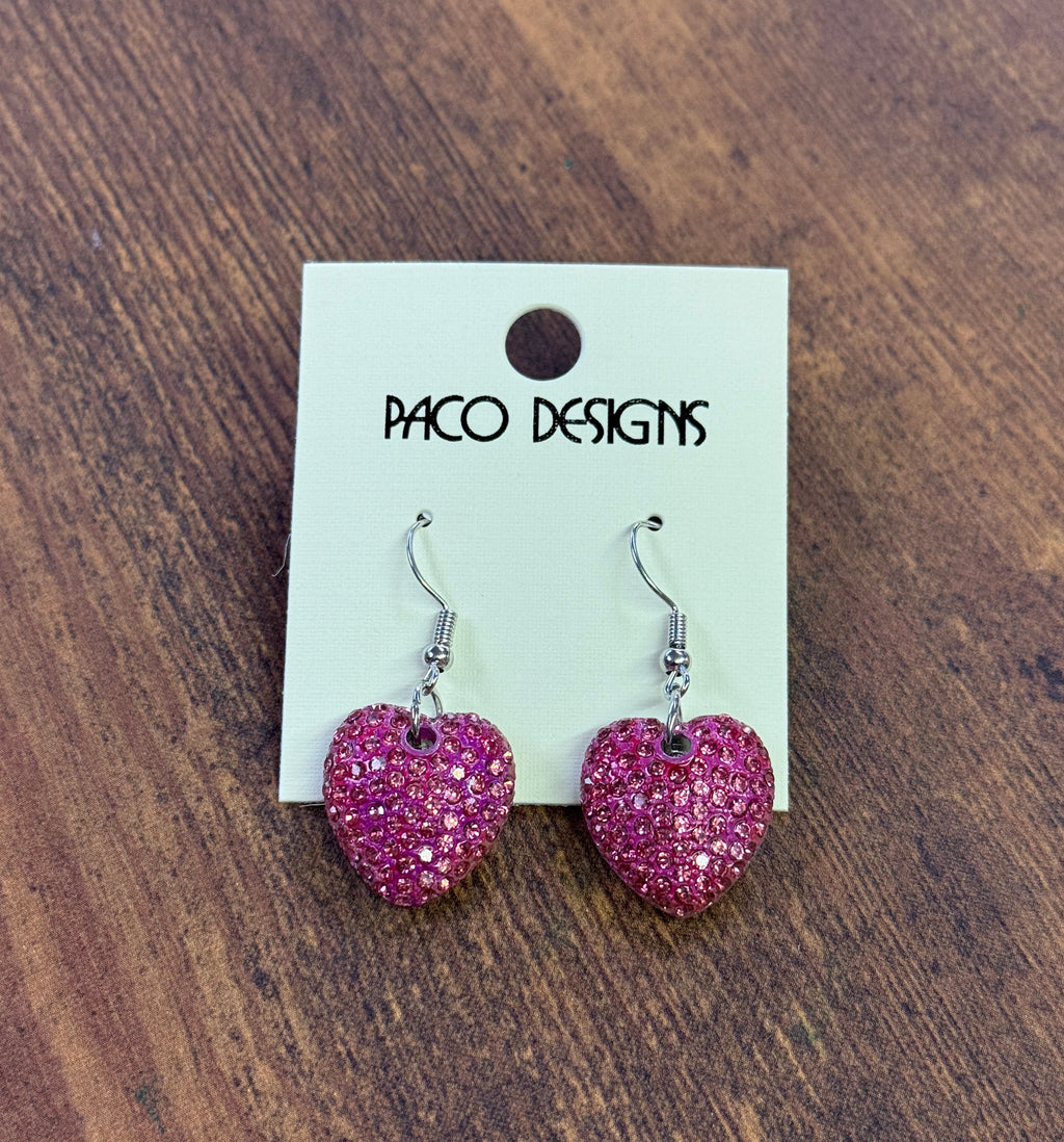 Pink heart-shaped earrings on a Paco Designs card against a wooden background