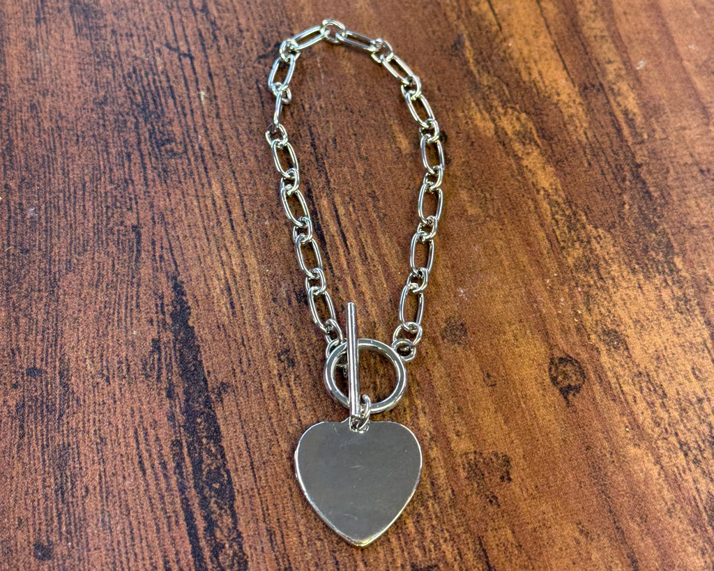 Silver chain bracelet with a heart-shaped charm on a wooden surface