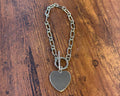 Silver chain bracelet with a heart-shaped charm on a wooden surface
