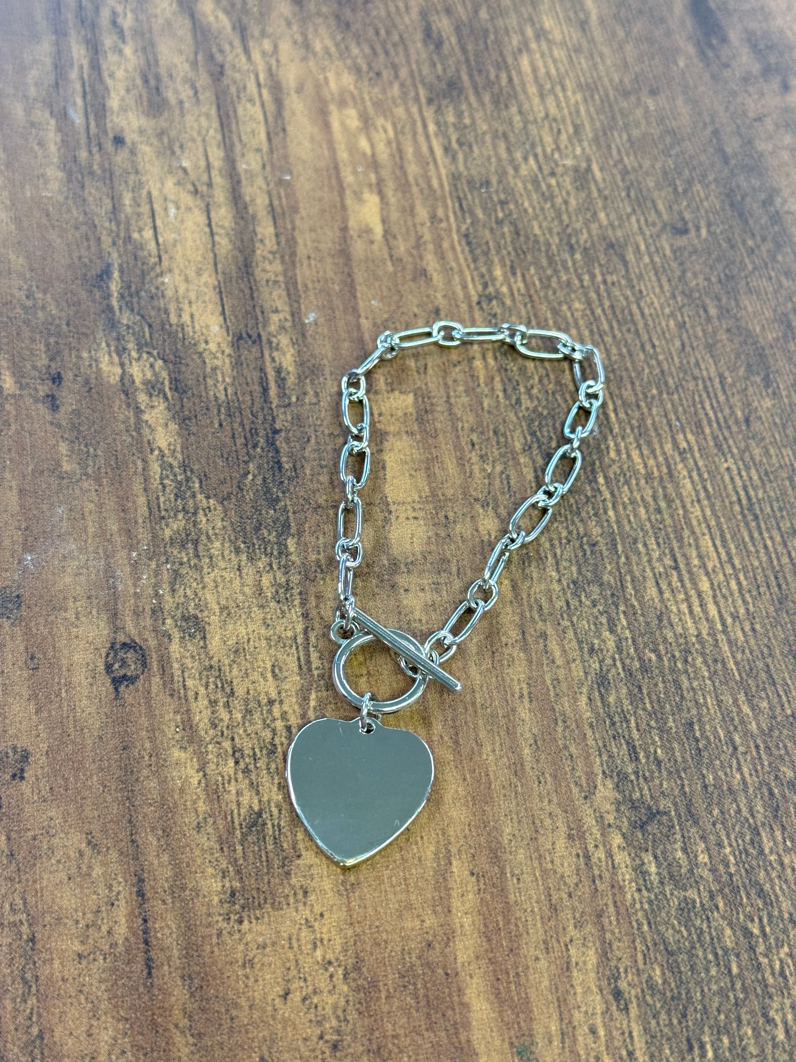 Silver chain bracelet with a heart-shaped tag on a wooden surface