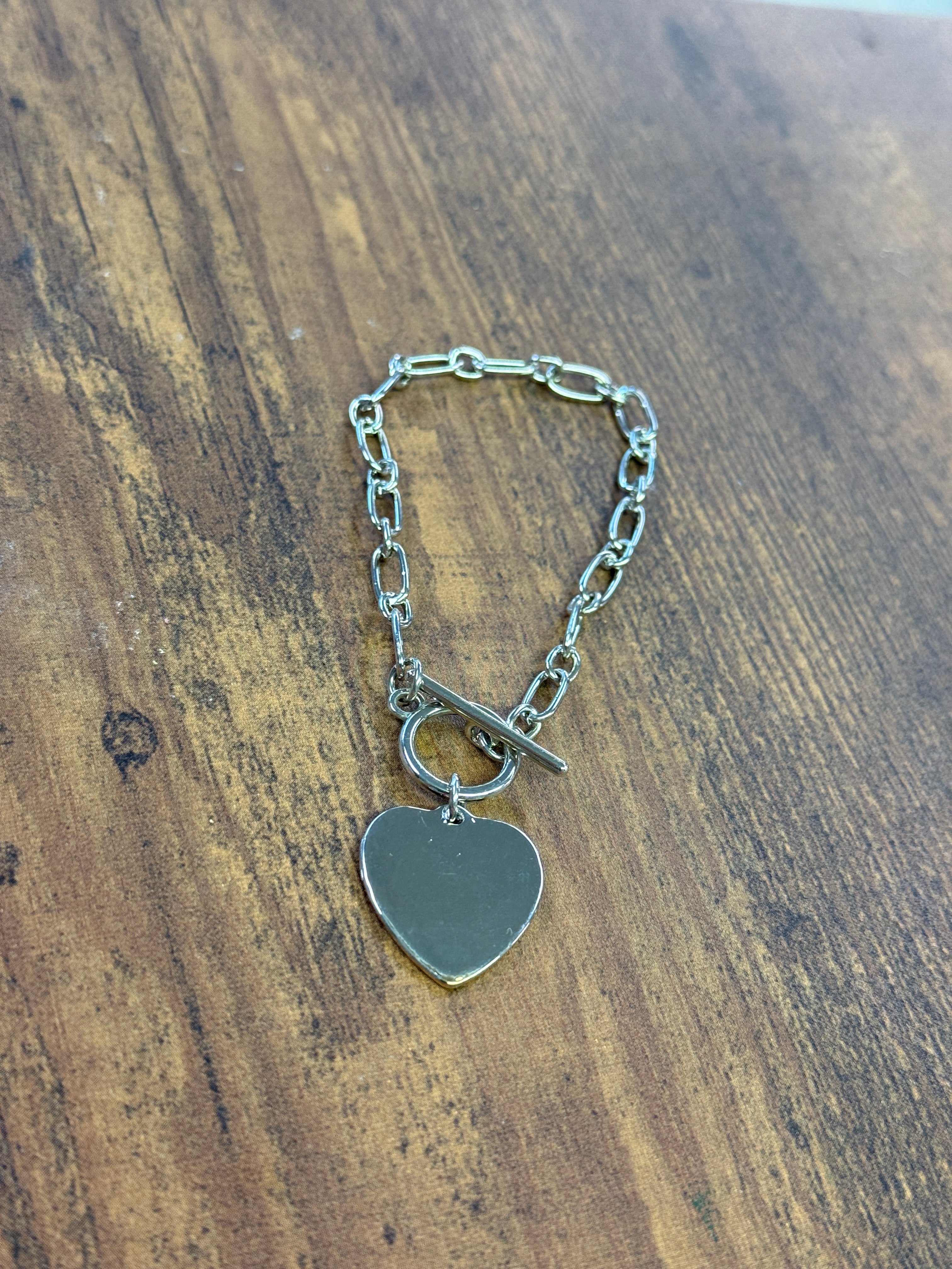 Silver chain bracelet with a heart-shaped tag on a wooden surface