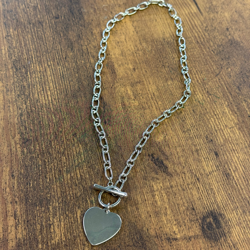 Silver chain necklace with a heart-shaped tag on a wooden surface