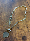 Silver chain necklace with a heart-shaped tag on a wooden surface